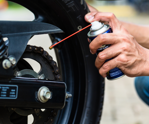 Motocyklista smaruje łańcuch w swojej maszynie smarem w sprayu.
