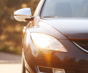 Na zdjęciu połowa czarnego samochodu. Pojazd ten ma włączone światła