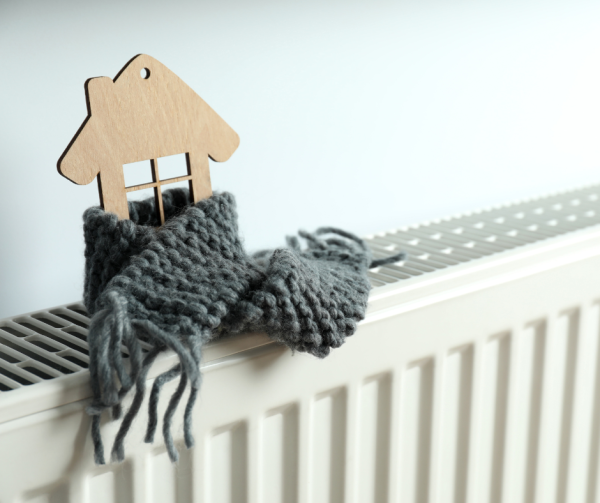 Na zdjęciu widać kaloryfer. Na nim stoi drewniany domek owinięty szarym szalikiem