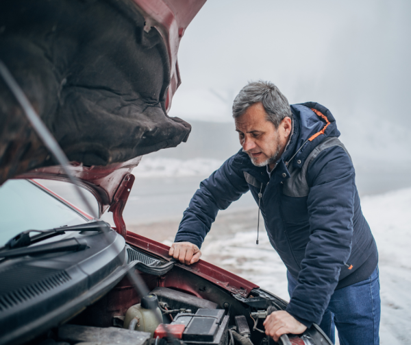 Mężczyzna otworzył maskę samochodu. Sprawdza, czy wszystko działa w pojeździe