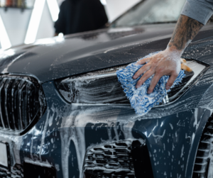 Mężczyzna myje samochód z użyciem detergentu i niebieskiej ścierki